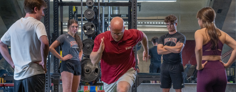 A man presents running. Four students standing and watching